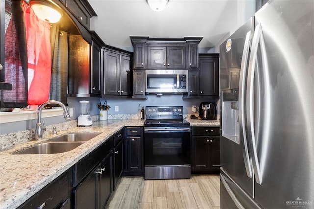 kitchen with sink, light stone countertops, stainless steel appliances, and light hardwood / wood-style flooring