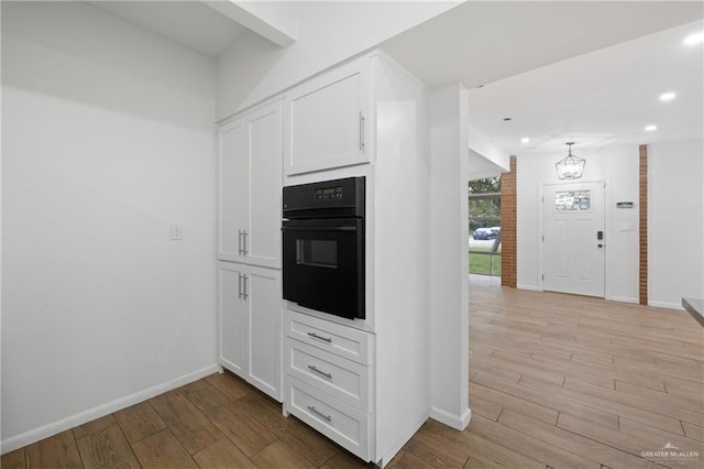 kitchen with black oven, light hardwood / wood-style flooring, white cabinets, and a notable chandelier