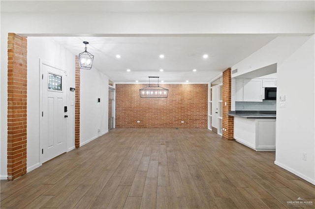 unfurnished living room featuring dark wood-type flooring, brick wall, and an inviting chandelier