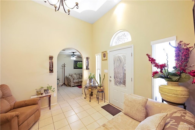 foyer entrance with ceiling fan with notable chandelier, light tile patterned floors, and a high ceiling