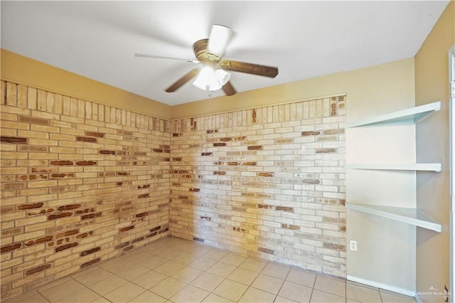 tiled empty room with ceiling fan and brick wall