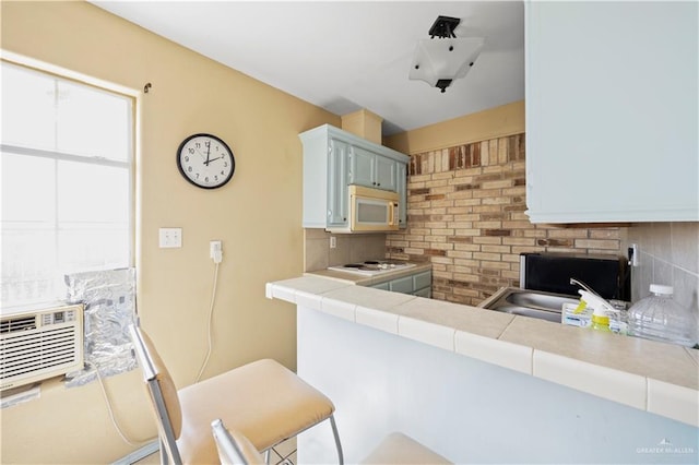 kitchen with tile counters, sink, kitchen peninsula, white appliances, and decorative backsplash