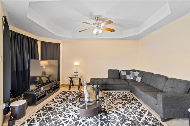 tiled living room with ceiling fan and a tray ceiling