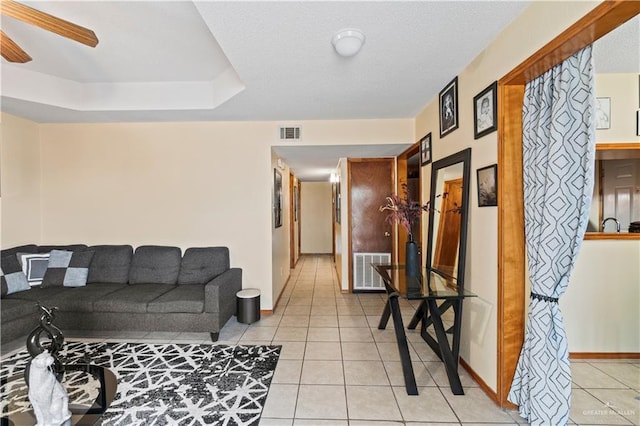 tiled living room with a tray ceiling and ceiling fan