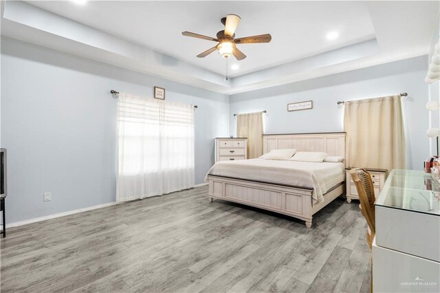 bedroom featuring a raised ceiling, baseboards, light wood finished floors, and ceiling fan