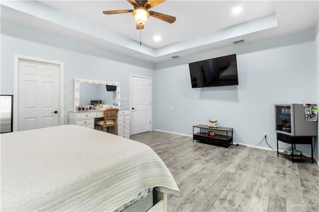 bedroom featuring a tray ceiling, light wood-style floors, visible vents, and baseboards