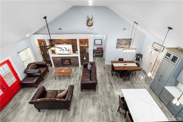 living room with a stone fireplace, high vaulted ceiling, a ceiling fan, and wood finished floors