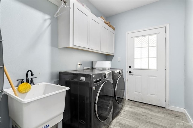 laundry area with baseboards, light wood finished floors, cabinet space, a sink, and independent washer and dryer