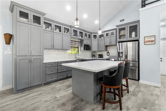 kitchen with tasteful backsplash, gray cabinetry, a center island, vaulted ceiling, and stainless steel fridge