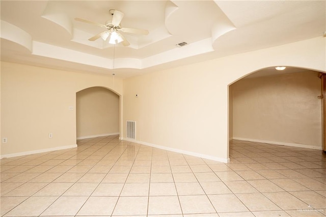 tiled empty room featuring a raised ceiling and ceiling fan