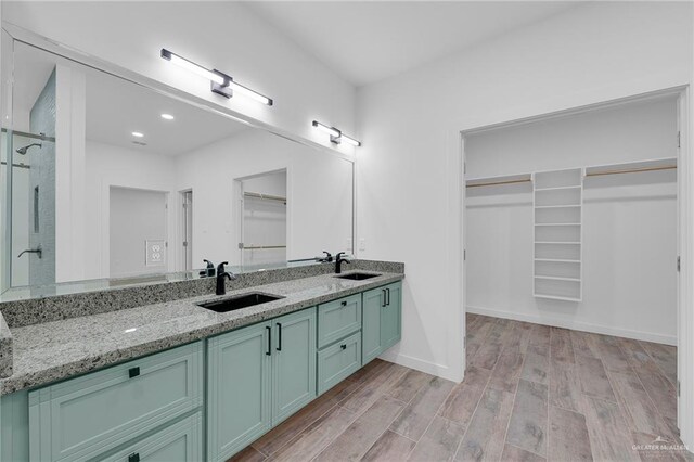 4720 Waterford Ave, Edinburg, TX 78539 - bathroom featuring a walk in closet, double vanity, wood finished floors, a stall shower, and baseboards