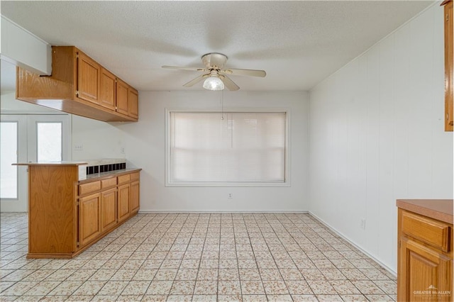 kitchen featuring a textured ceiling, brown cabinets, light countertops, and a ceiling fan