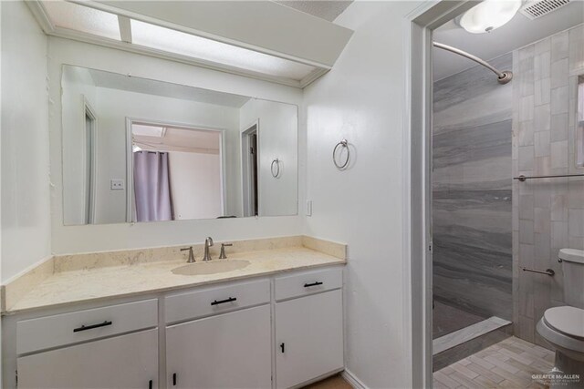 full bathroom featuring vanity, visible vents, a tile shower, and toilet