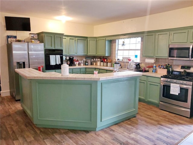 kitchen with tile countertops, green cabinetry, and appliances with stainless steel finishes