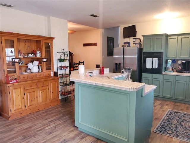 kitchen with stainless steel refrigerator with ice dispenser, oven, tile counters, and hardwood / wood-style floors