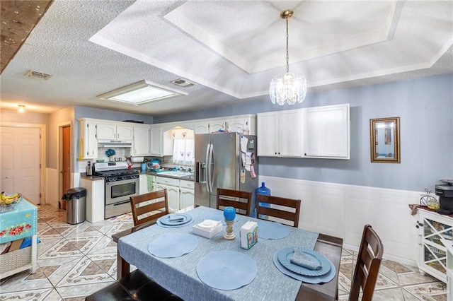 510 S 9th St, Hidalgo, TX 78557 - dining space with a raised ceiling, a chandelier, a textured ceiling, light tile patterned floors, and a wainscoted wall