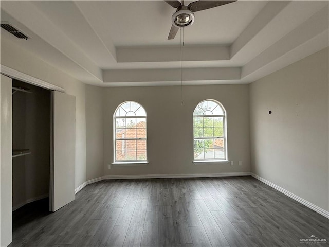 empty room with dark hardwood / wood-style flooring, a raised ceiling, ceiling fan, and a healthy amount of sunlight