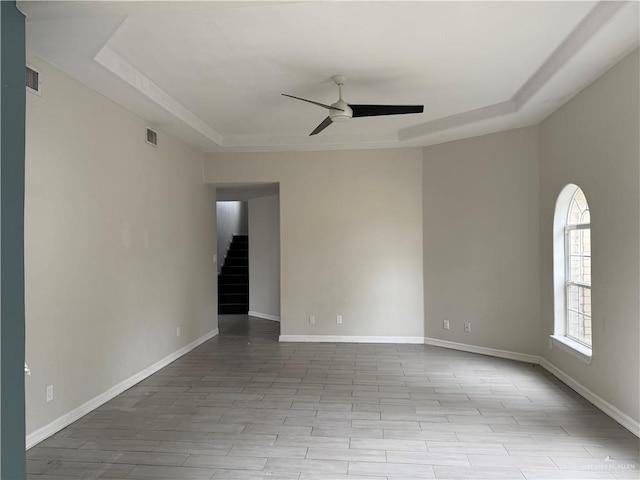 empty room featuring ceiling fan, light hardwood / wood-style flooring, and a tray ceiling