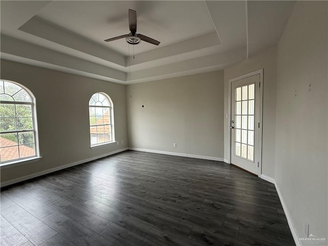 empty room with dark hardwood / wood-style floors, ceiling fan, and a tray ceiling