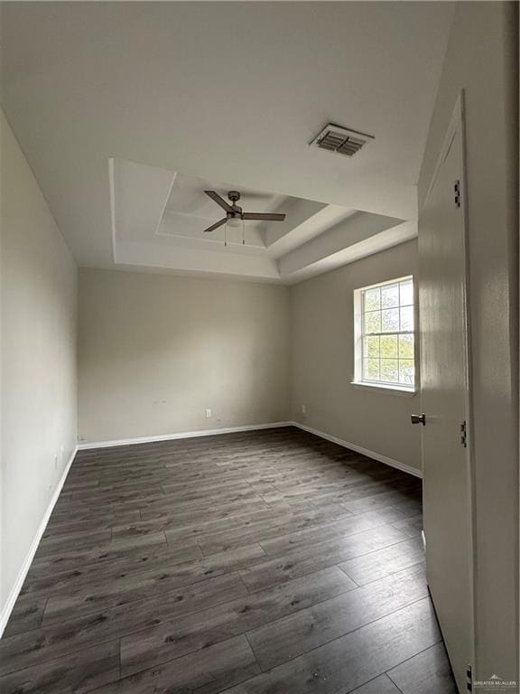 unfurnished room featuring a raised ceiling, ceiling fan, and dark hardwood / wood-style floors