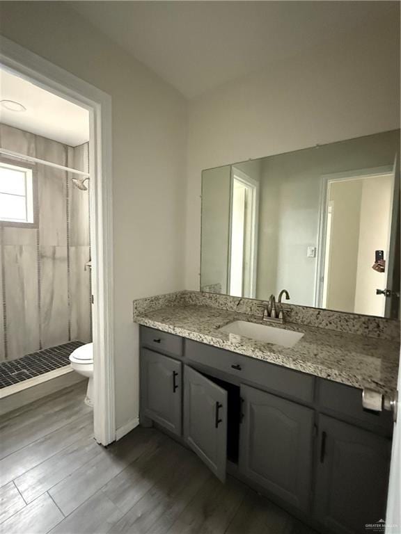 bathroom with hardwood / wood-style floors, vanity, toilet, and a tile shower