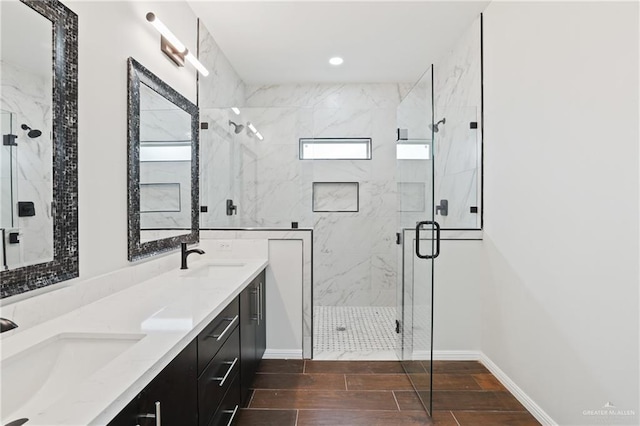 full bath with a marble finish shower, double vanity, a sink, and baseboards