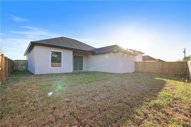 back of house with stucco siding, a lawn, roof with shingles, and a fenced backyard
