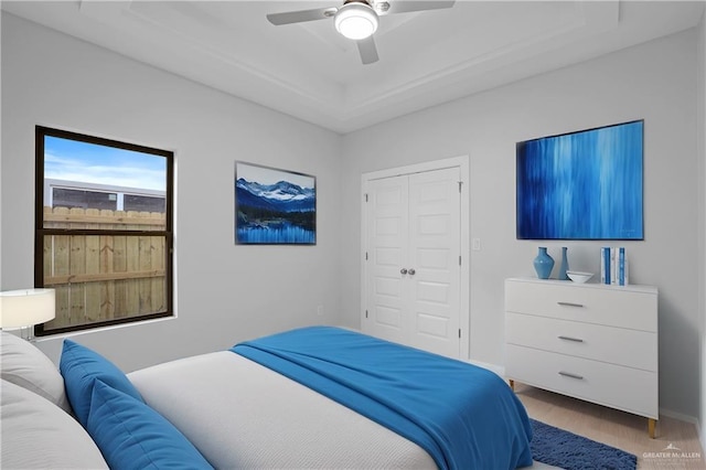 bedroom featuring wood finished floors, baseboards, a tray ceiling, ceiling fan, and a closet