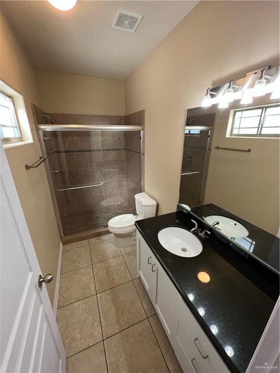 bathroom with tile patterned flooring, vanity, a shower with door, and toilet