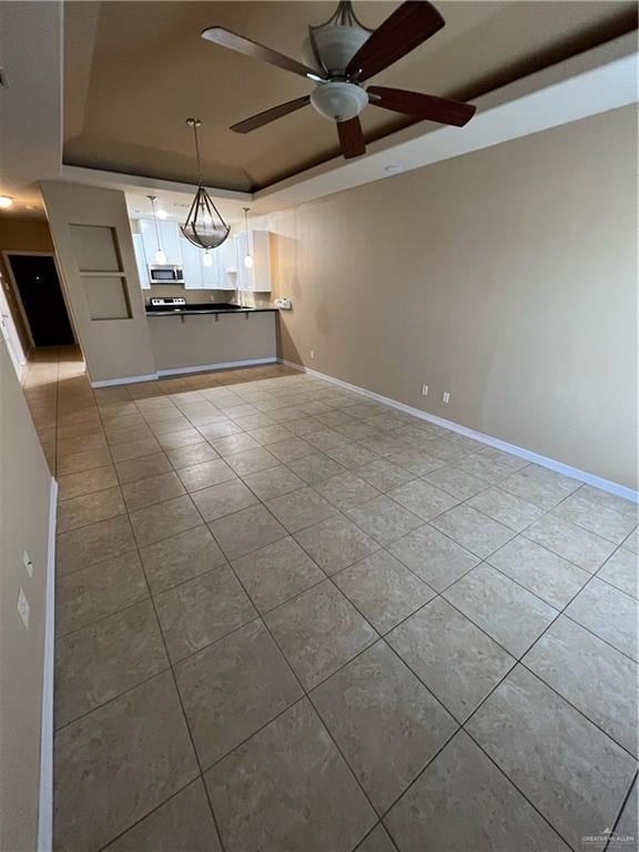 interior space with a tray ceiling, ceiling fan, and light tile patterned flooring