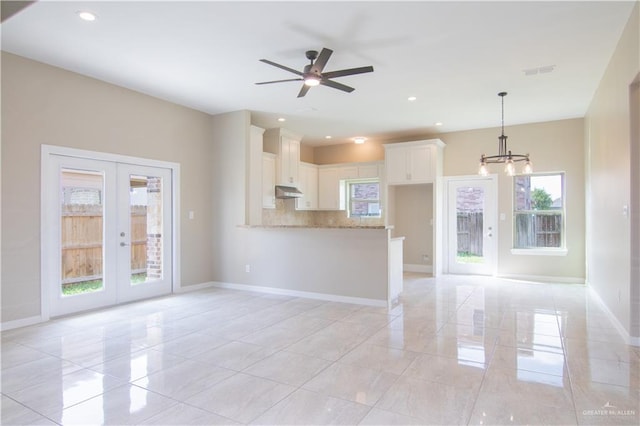 unfurnished living room featuring french doors and ceiling fan with notable chandelier