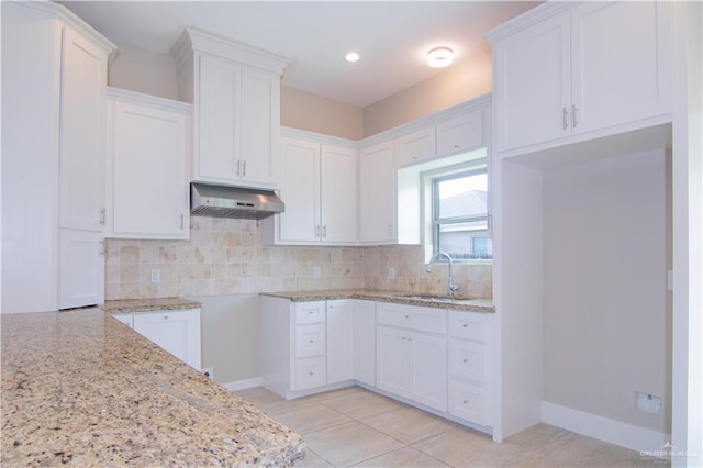 kitchen featuring backsplash, light stone countertops, white cabinetry, and sink