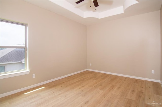 empty room featuring a raised ceiling, light hardwood / wood-style flooring, and ceiling fan