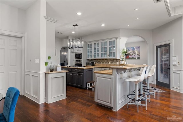 kitchen featuring gray cabinetry, a breakfast bar, dark wood-type flooring, kitchen peninsula, and stainless steel appliances