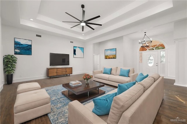 living room with dark hardwood / wood-style floors, ceiling fan with notable chandelier, and a tray ceiling