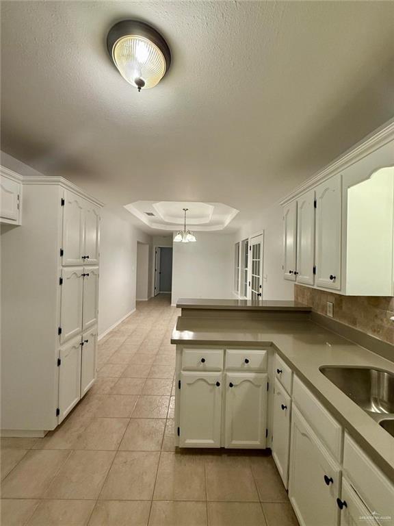 kitchen with a peninsula, white cabinetry, light tile patterned floors, and a raised ceiling