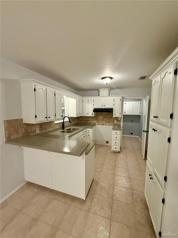 kitchen featuring tasteful backsplash, a sink, white cabinets, a peninsula, and visible vents