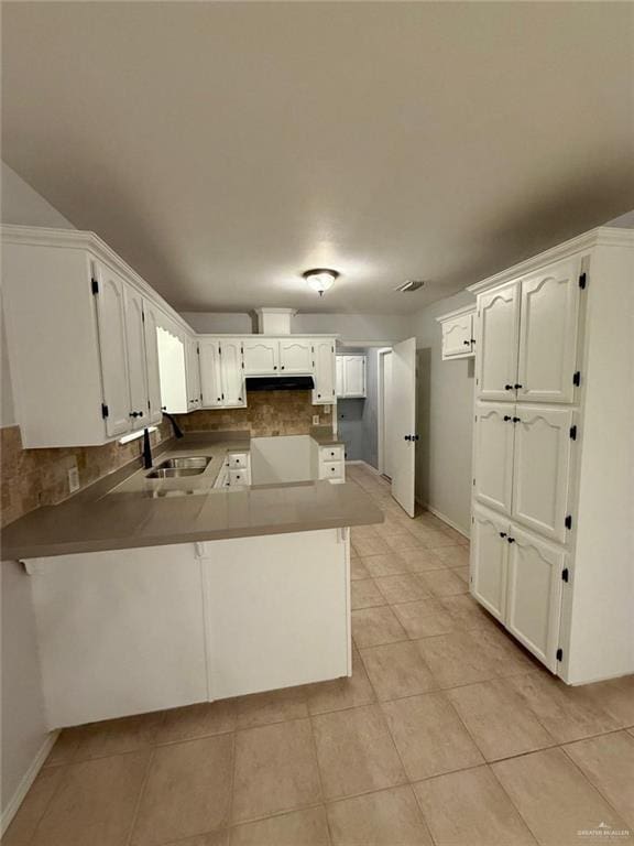 kitchen featuring a sink, light tile patterned flooring, decorative backsplash, a peninsula, and white cabinetry
