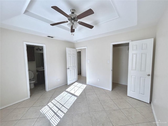 unfurnished bedroom with a tray ceiling, ensuite bath, and a closet