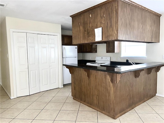 kitchen featuring kitchen peninsula, dark brown cabinets, light tile patterned floors, and white appliances