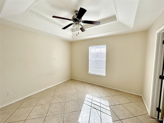 empty room with ceiling fan, a raised ceiling, and light tile patterned floors