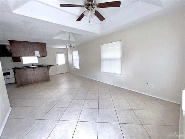 unfurnished living room with ceiling fan with notable chandelier, light tile patterned floors, and a tray ceiling