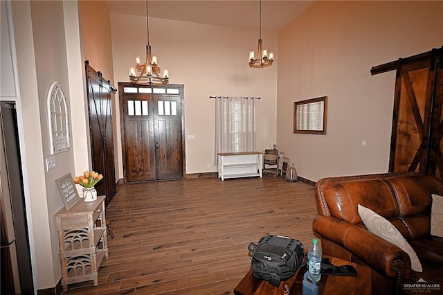 entryway featuring a barn door, dark wood-type flooring, high vaulted ceiling, and an inviting chandelier