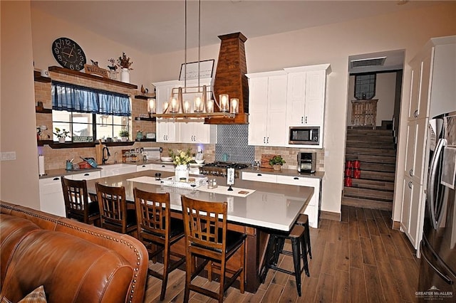 kitchen featuring hanging light fixtures, an island with sink, a kitchen bar, white cabinets, and appliances with stainless steel finishes