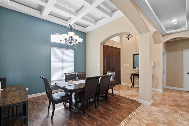 dining room featuring baseboards, arched walkways, a towering ceiling, wood finished floors, and a notable chandelier