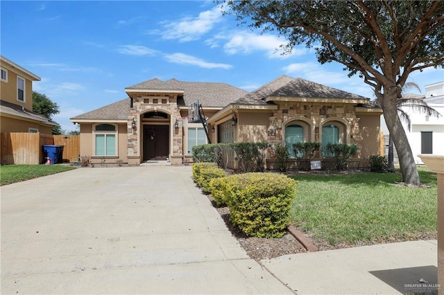 view of front of property with fence, driveway, stone siding, stucco siding, and a front yard