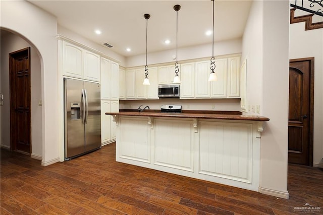 kitchen featuring decorative light fixtures, a kitchen bar, kitchen peninsula, stainless steel appliances, and dark wood-type flooring