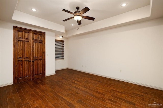 unfurnished bedroom with ceiling fan, dark hardwood / wood-style flooring, and a raised ceiling