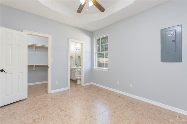 unfurnished bedroom featuring a walk in closet, electric panel, a raised ceiling, and ceiling fan