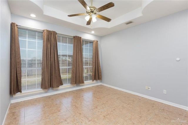 tiled spare room with ceiling fan and a raised ceiling